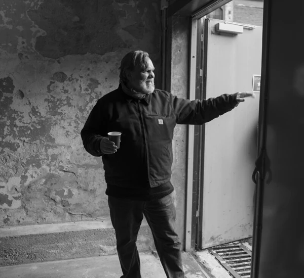 Forfatter Lars Ove Seljestad står i en døråpning i et gammelt fabrikklokale og peker ut døren. Foto.